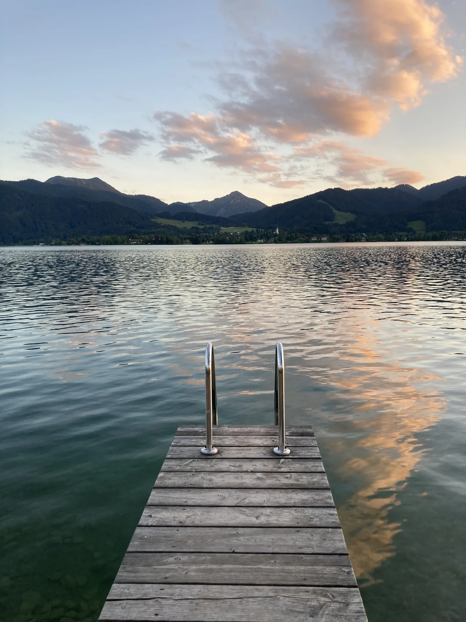 Holzsteg im stillen Tegernsee in der Abenddämmerung, dahinter die Berge